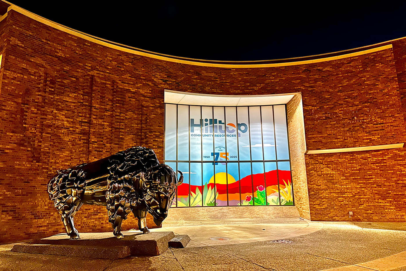 Nighttime photo of exterior of brick building with buffalo statue 