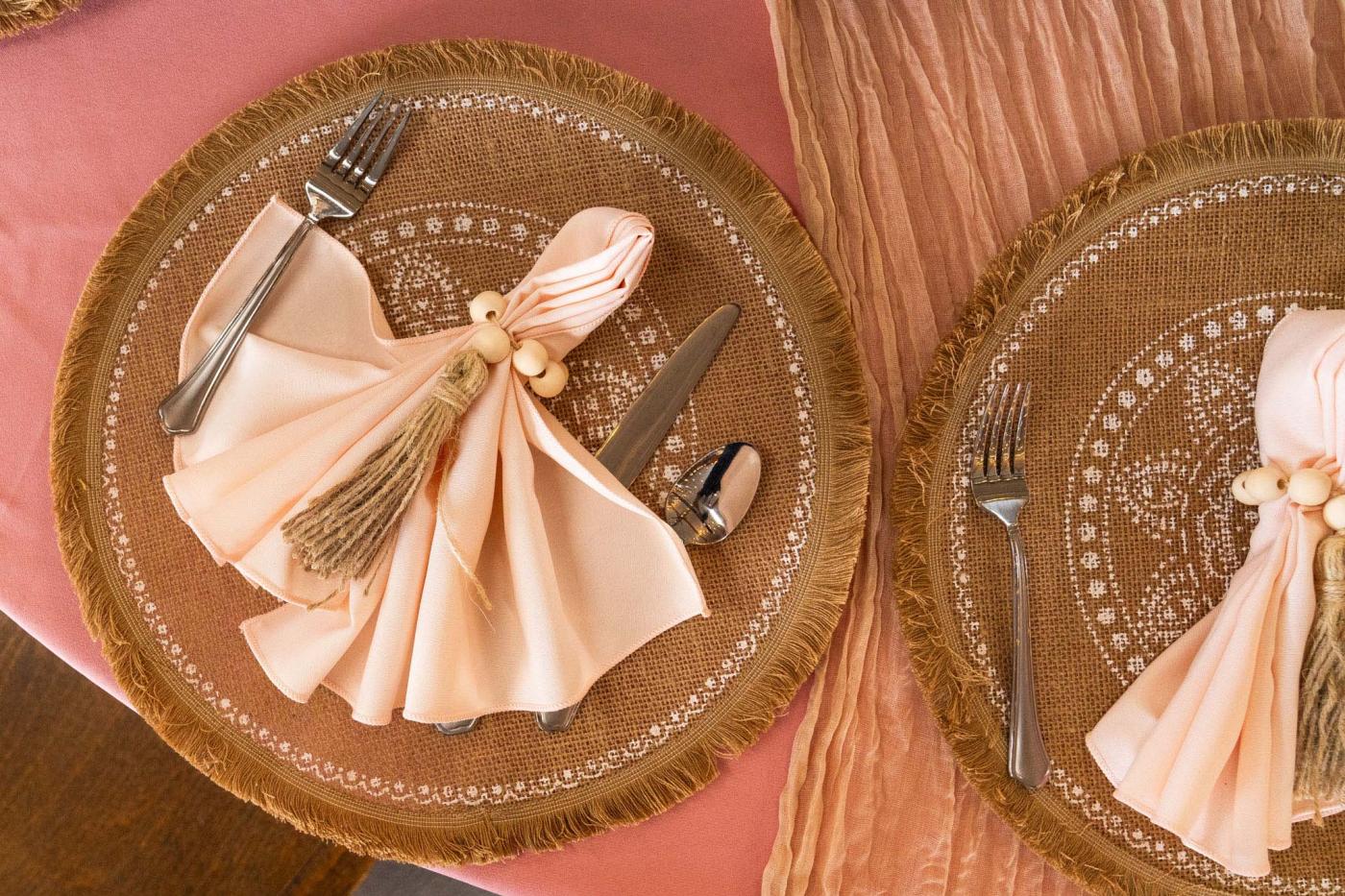 Place setting with pink table cloth, burlap round place settings, and a pink napkin folded fancily