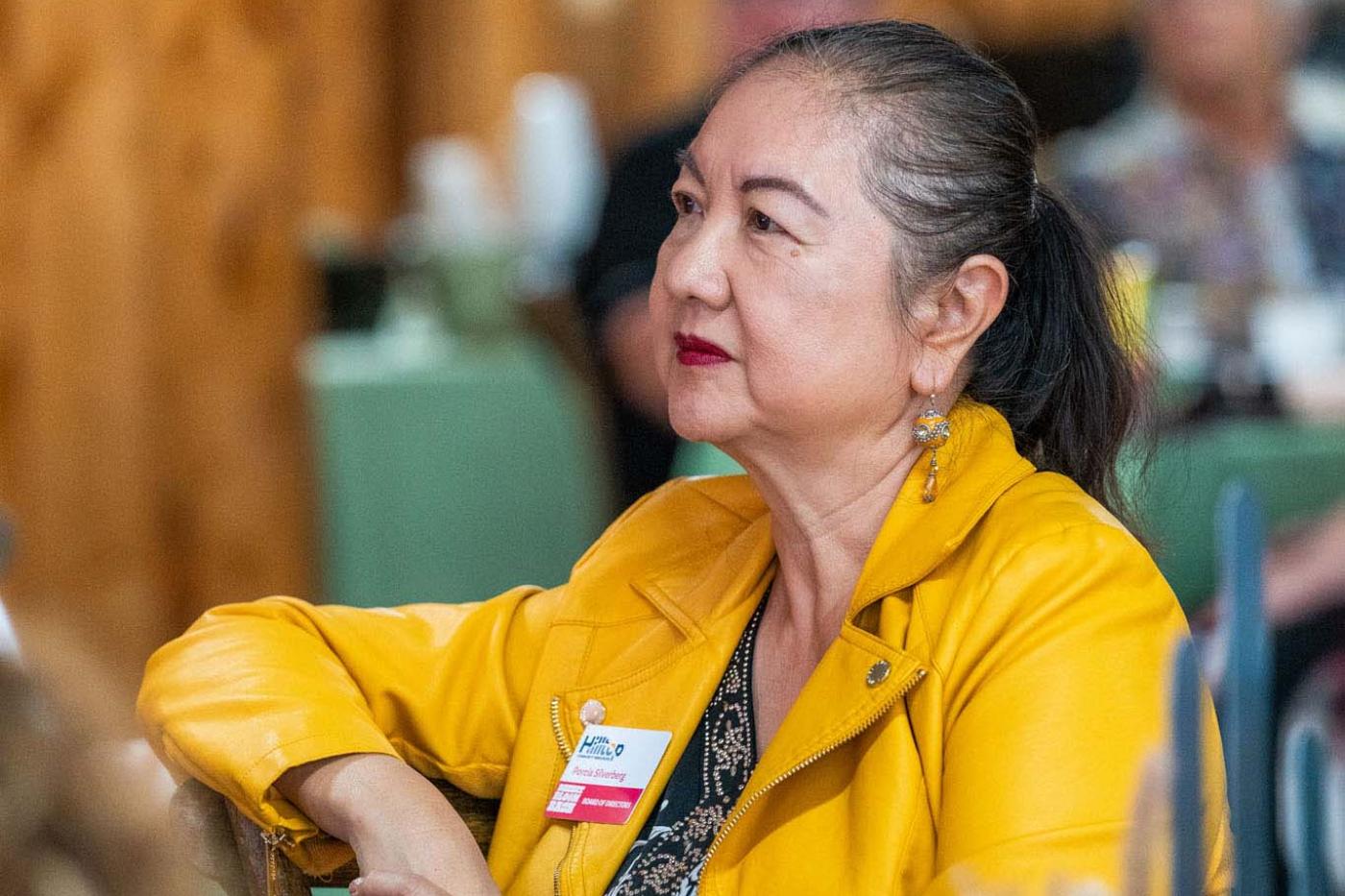 Woman in yellow jacket in audience, watching presentation on stage