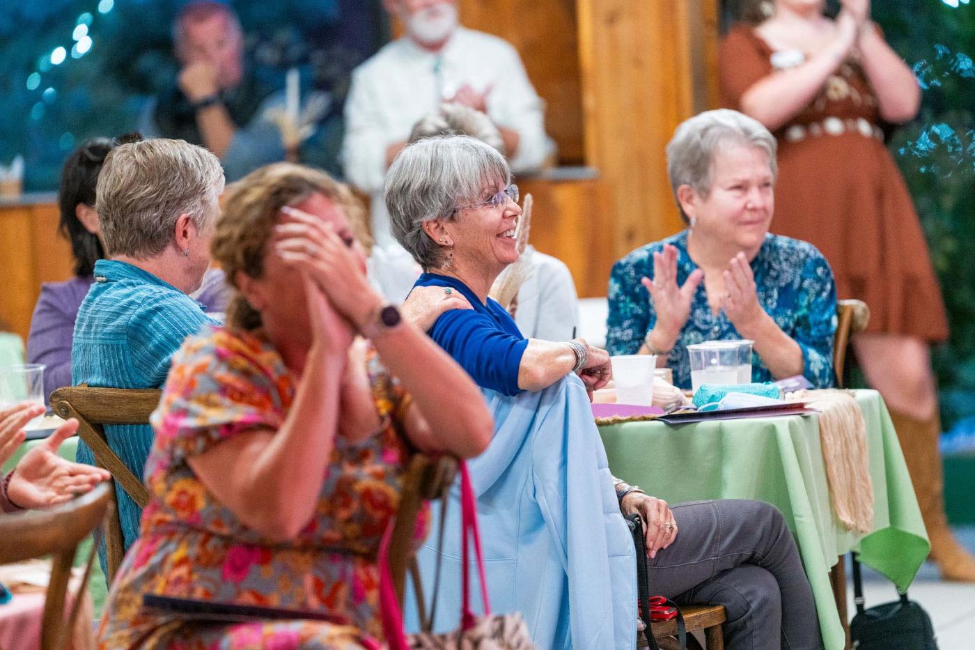 Women in audience smiling, raising bidder paddle