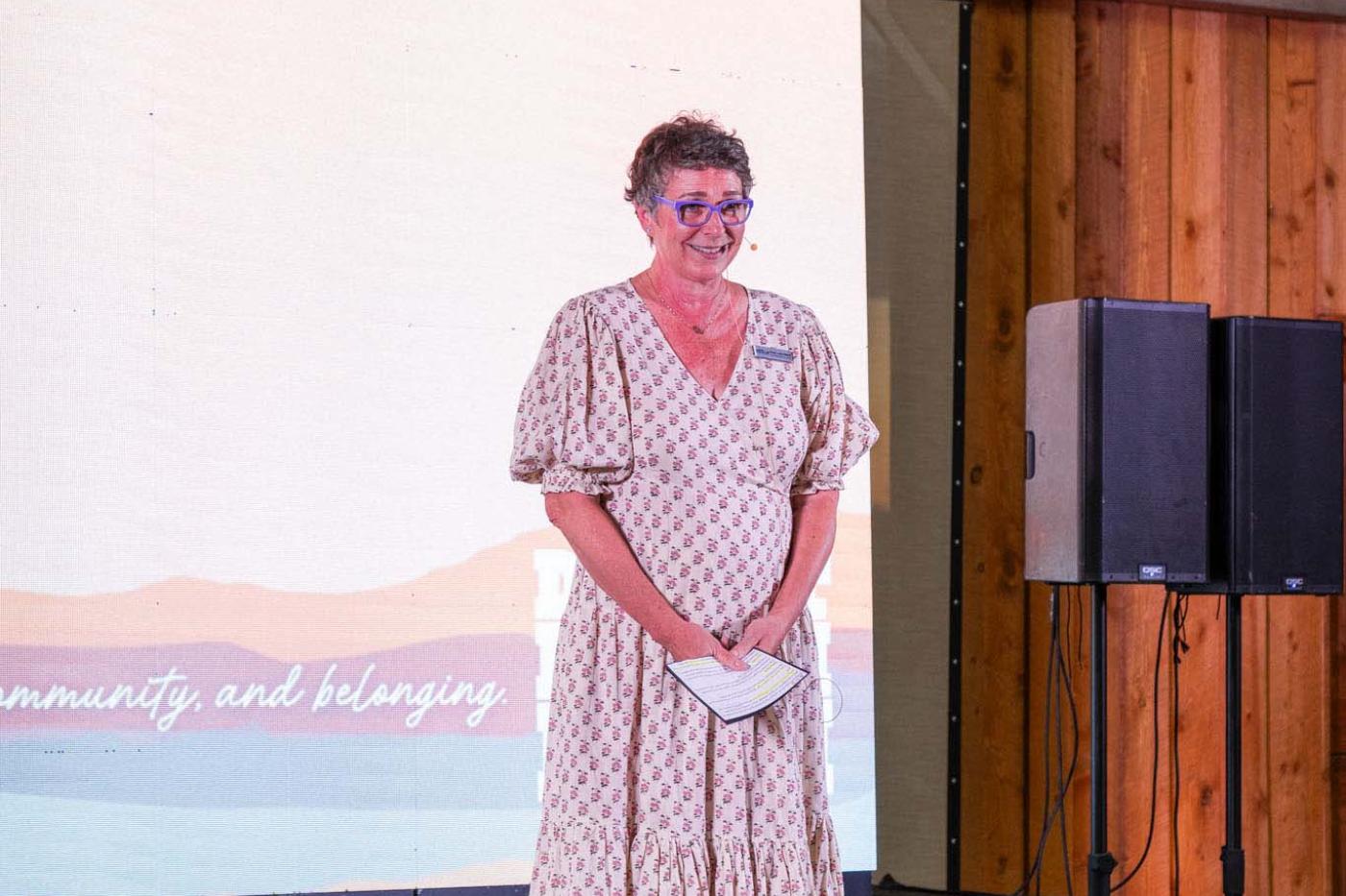 Woman on stage with short hair and glasses giving a speech