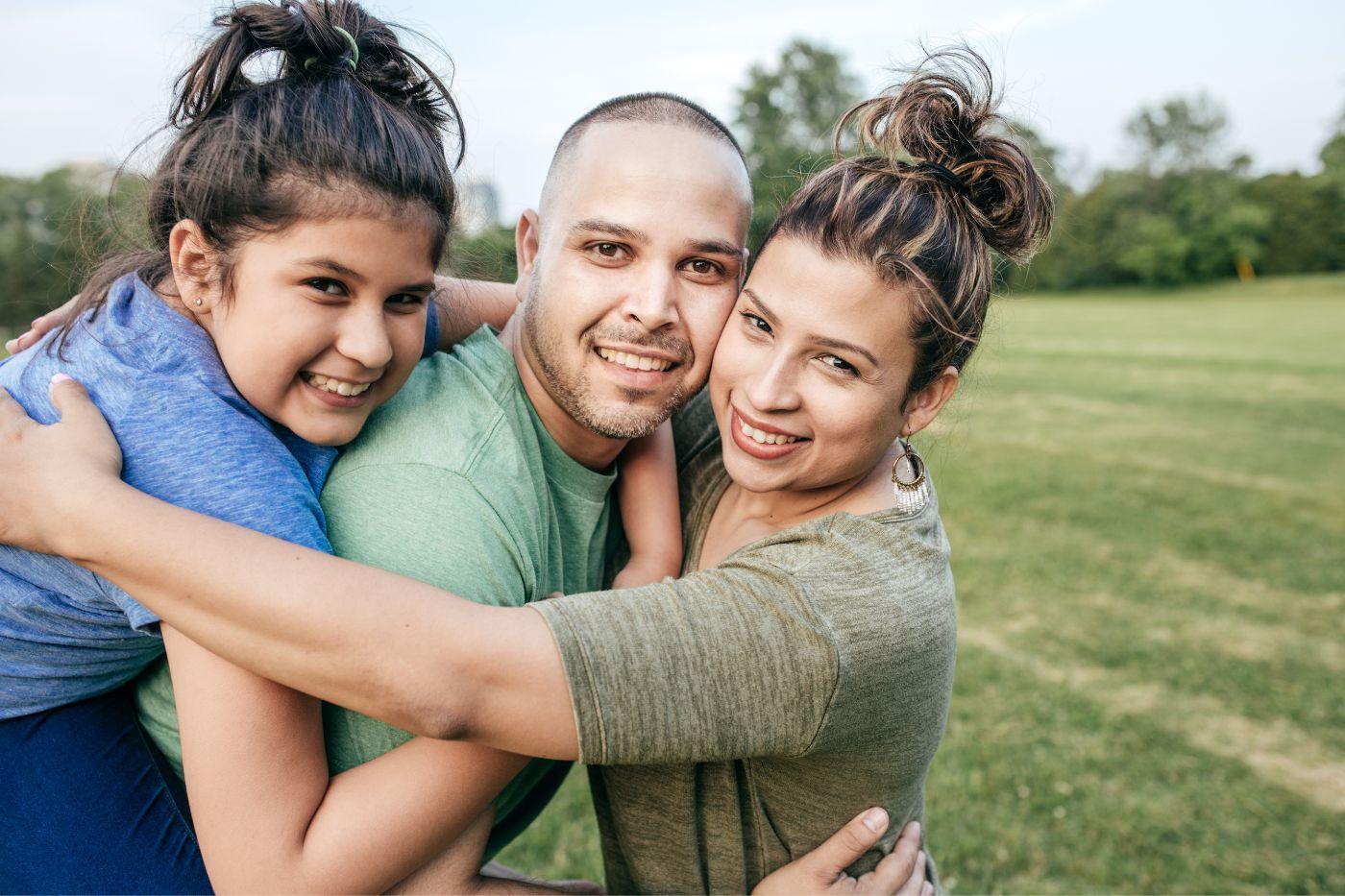 Mother, father, and daughter hugging outside and smiling at camera