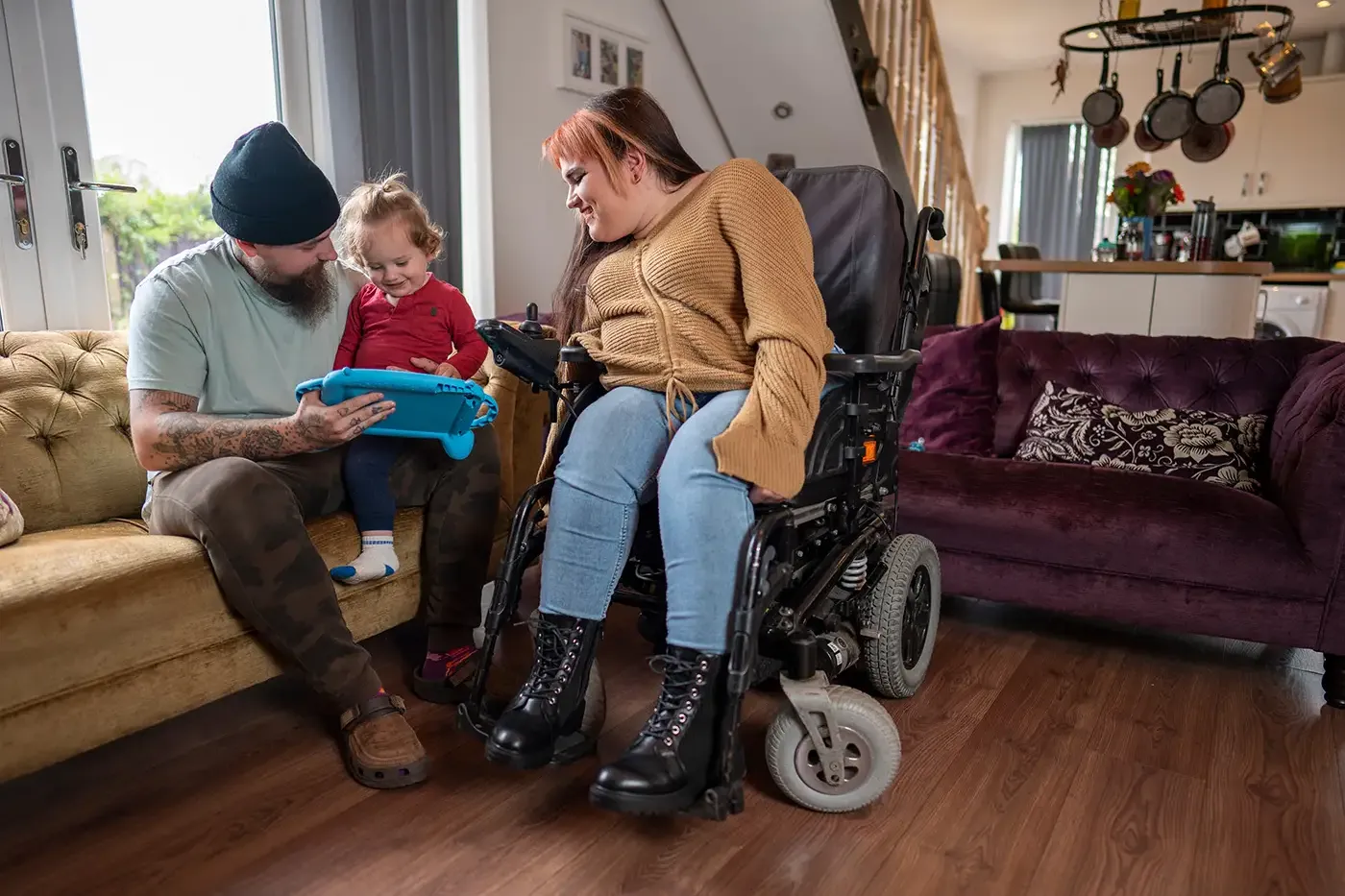 A family sitting together at home, including a parent using a wheelchair, as they support their young child—reflecting the kind of stability, safety, and assistance Hilltop’s Housing Support programs work to help families achieve during housing transitions.