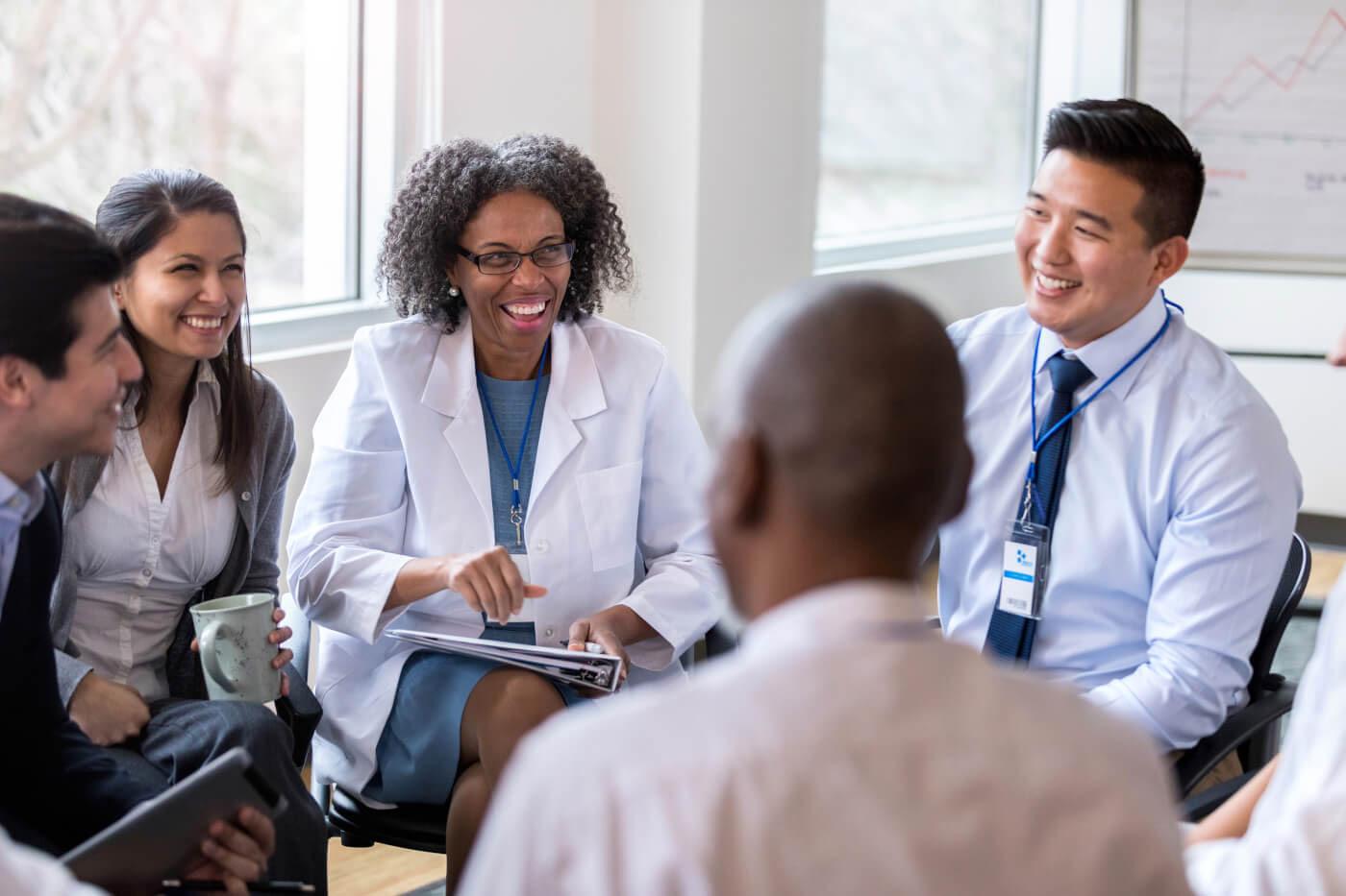 A diverse group of healthcare and community service professionals seated in a circle, smiling and engaged in discussion during a collaborative meeting.